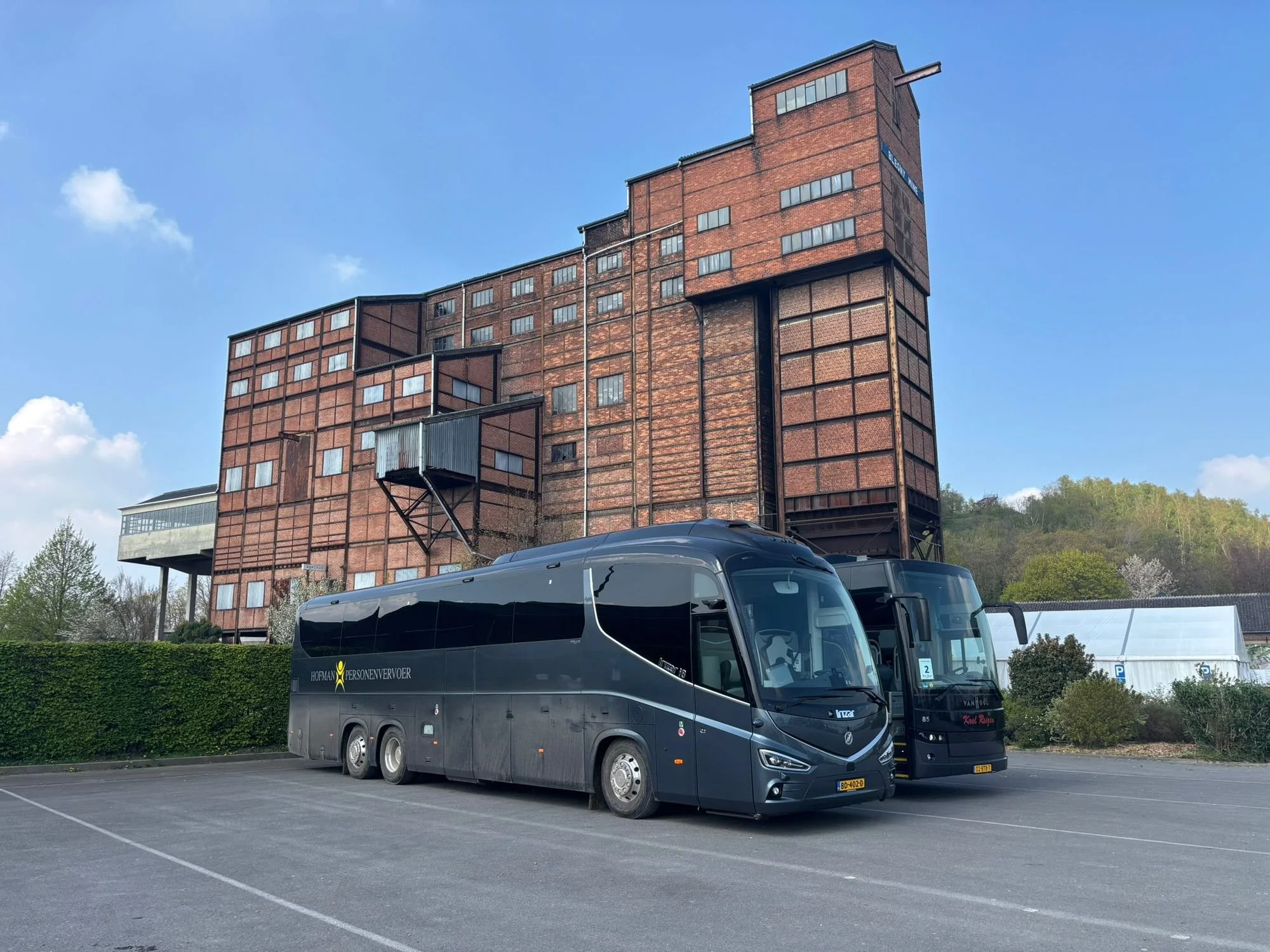 Touringcars van Hofman Personenvervoer bij een industrieel gebouw